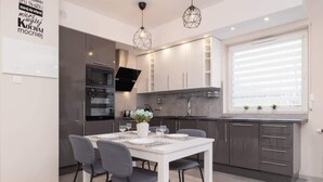 Una cocina moderna con armarios blancos, un horno negro y una zona de comedor con una mesa blanca y sillas grises.