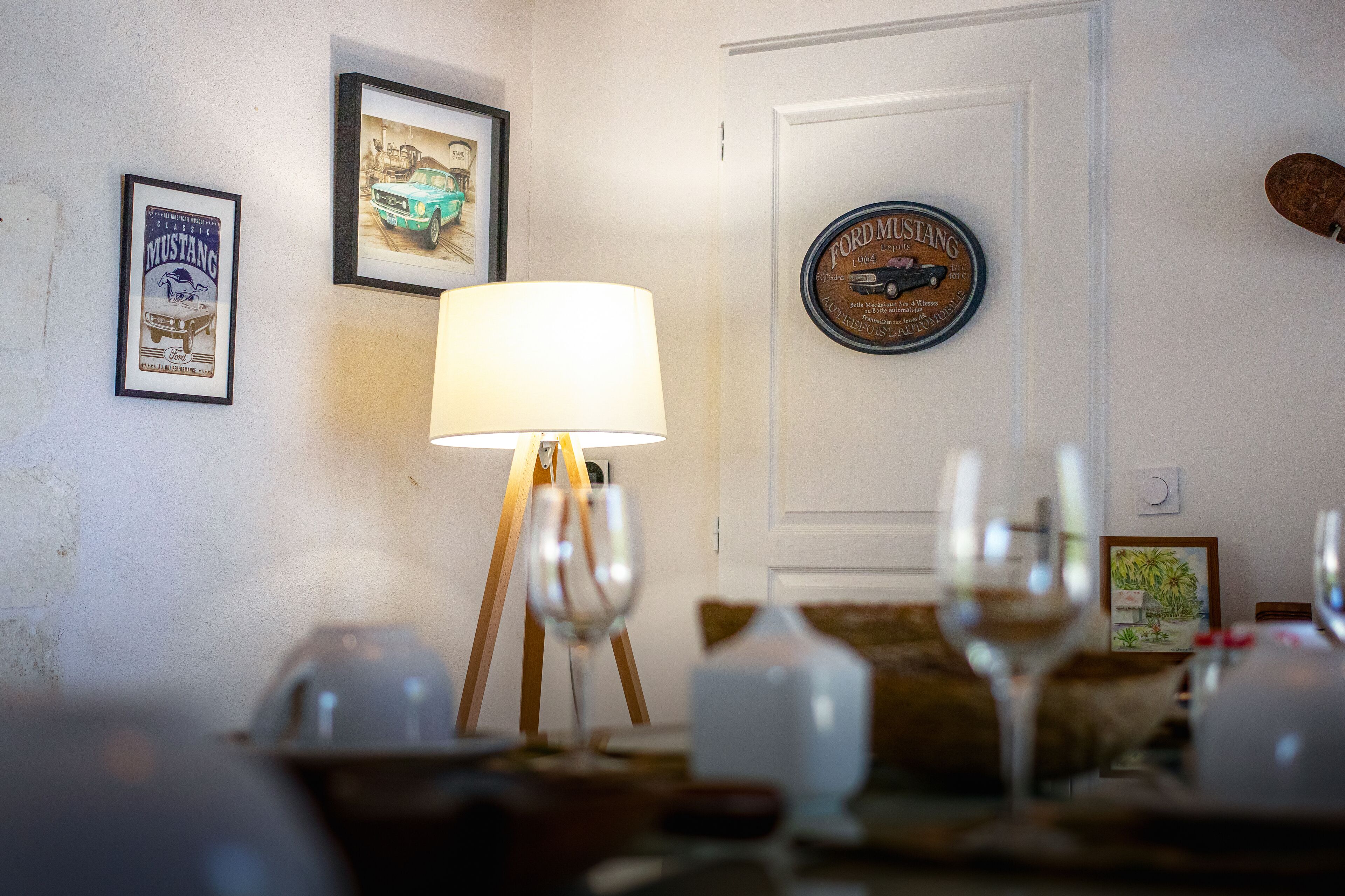 Ein Essbereich mit einem Tisch für zwei Personen, einer Lampe und gerahmten Automobilia an der Wand.