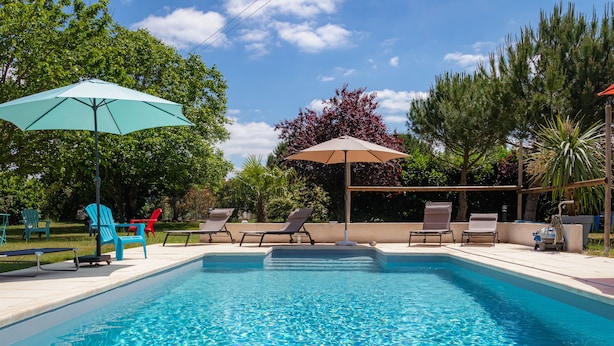 Piscina com espreguiçadeiras e guarda-sóis, rodeada por árvores e um céu claro.