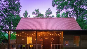 Une cabane rustique dotée d’une véranda, de guirlandes lumineuses et d’une enseigne indiquant qu’il s’agit d’un établissement proposant l’hébergement et le petit-déjeuner.