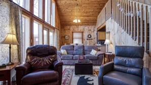 A cozy living room with a leather sofa, a black leather chair, and a wooden staircase with a decorative railing. - Private Setting,Hot Tub, Whirlpool, Centrally Located, Minutes to Smoky Mtn Park (Sevierville)