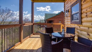 Una terraza de madera con mobiliario de mimbre y una mesa, con vistas a un edificio con techo verde.