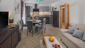 A modern living room with a sofa, a coffee table with fruit, a dining area with chairs, a kitchen with cabinets, and a TV on a stand. - Lovely apartment in Micetici (Micetici)