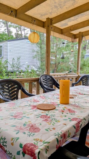 An outdoor patio with a table covered in a floral tablecloth, surrounded by chairs.
