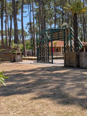 A playground area with a green climbing structure, surrounded by trees and a building with a red roof.