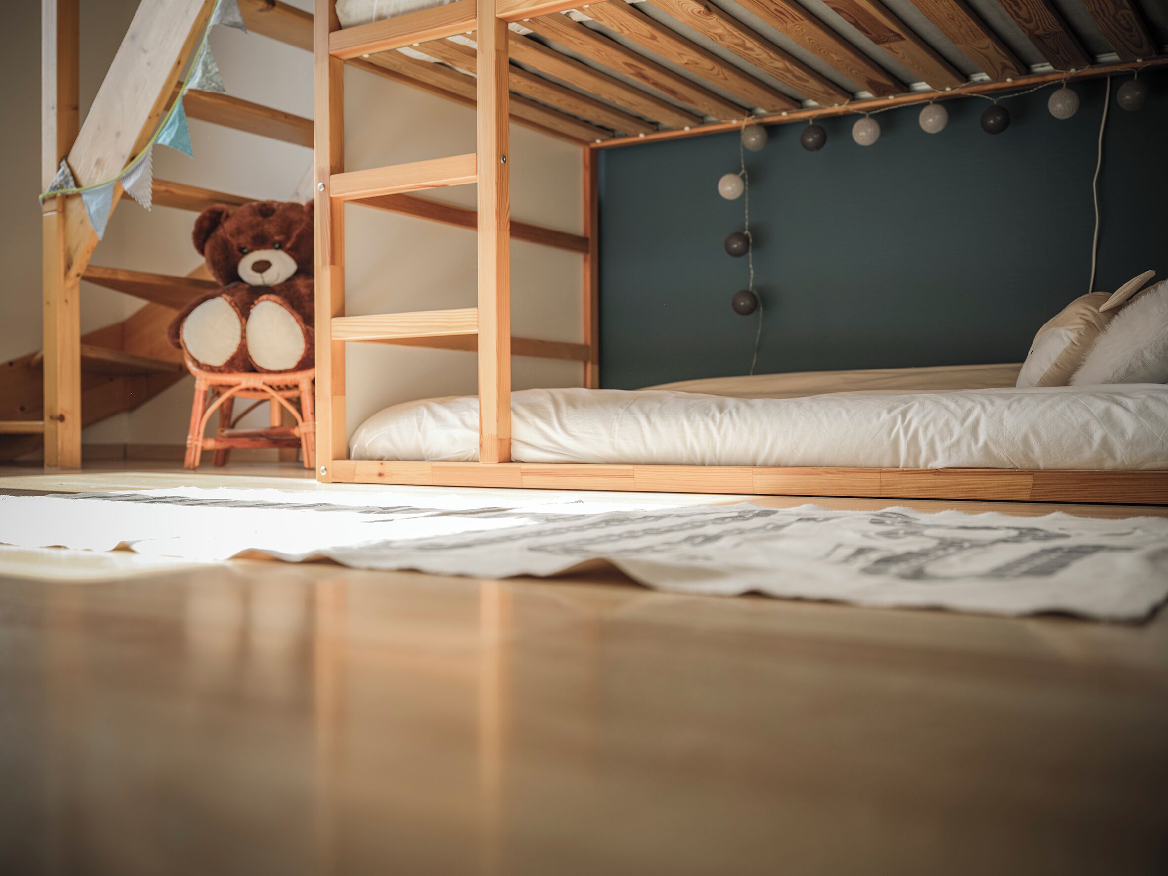 A wooden bunk bed with a green headboard, a teddy bear, and a small chair.