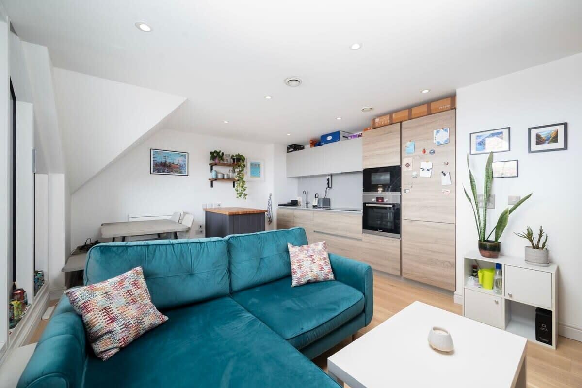 Een moderne woonkamer met een blauwgroene bank, een witte salontafel en een keuken op de achtergrond.