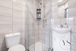 Un baño moderno con ducha de vidrio, inodoro y lavamanos con espejo.