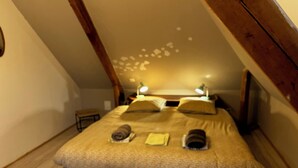 Une chambre confortable avec un plafond en pente, un lit avec des oreillers et une serviette roulée, et une petite table de chevet.