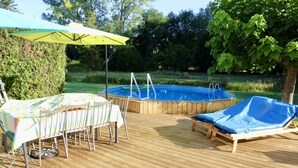 Une terrasse extérieure avec une piscine, une table et des chaises, ainsi qu’un fauteuil de relaxation.