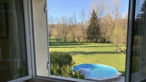 Une vue à travers une fenêtre donnant sur une cour arrière avec une piscine, une pelouse verdoyante et des arbres.