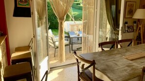 Un coin repas avec une table et des chaises, une vue sur un jardin par une porte vitrée et un tableau accroché au mur.