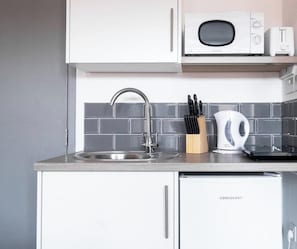 A kitchen with a stainless steel sink, a microwave, a toaster, and a kettle.