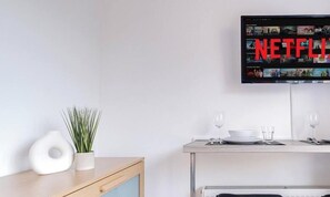 A modern living room with a flat-screen TV mounted on the wall displaying a Netflix interface.