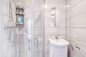 A modern bathroom with a glass shower enclosure, a white sink, and a mirror.