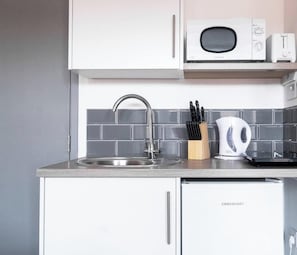 A kitchen with a stainless steel sink, a microwave, a toaster, and a kettle.