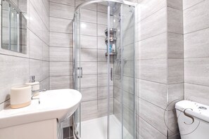 A modern bathroom with a glass-enclosed shower, a white sink, and a toilet.