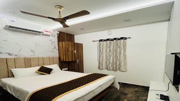 A modern hotel room with a bed, a ceiling fan, a TV, and a wooden wardrobe. - The Tendo Inn (Pollachi)