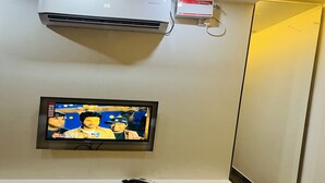 A television mounted on a wall with a ceiling air conditioner and a small device above it. - The Tendo Inn (Pollachi)