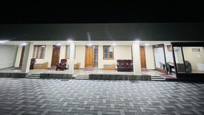 A hotel entrance with a tiled pavement, wooden doors, and a seating area with chairs and a sofa. - The Tendo Inn (Pollachi)
