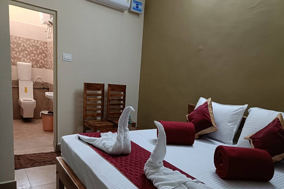 Habitación de hotel con cama, dos sillas de madera, baño visible a través de una puerta abierta y aire acondicionado de pared.