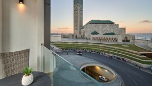 Una vista di un edificio storico con un'alta torre e una struttura con tetto verde, una rotatoria e un corpo d'acqua sullo sfondo.