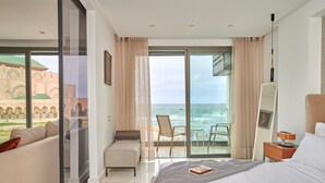 Una camera d'albergo con un letto, un divano, una sedia, un tavolino e vista sull'oceano.