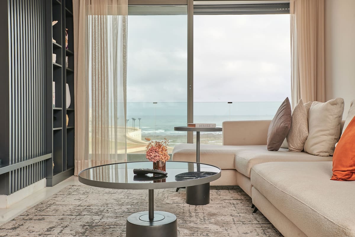 A modern living room with a glass coffee table, a sofa, and a view of the ocean.