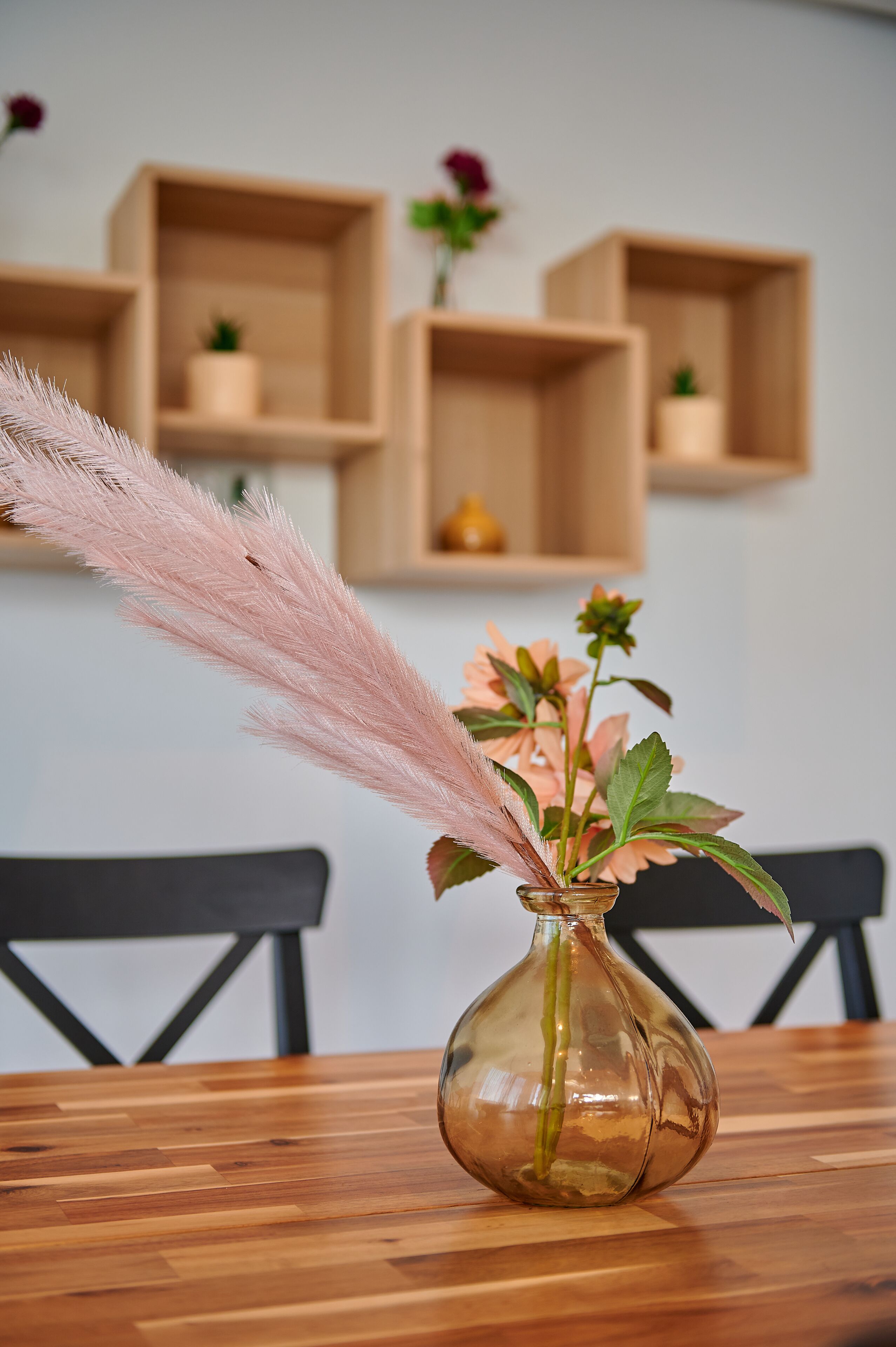 A clear view of a wooden dining table with a glass vase containing pink flowers and a feather.