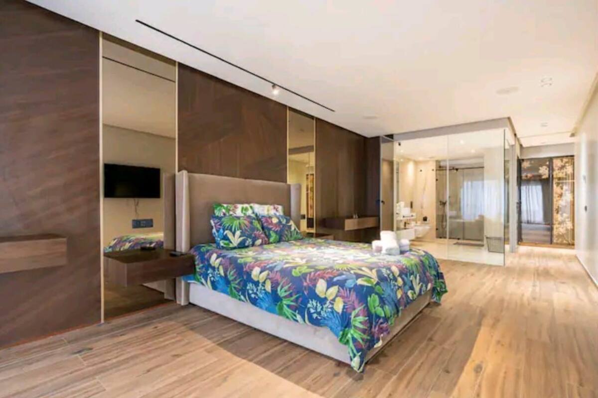 A modern bedroom with a large bed, a TV, and a glass door leading to a bathroom.