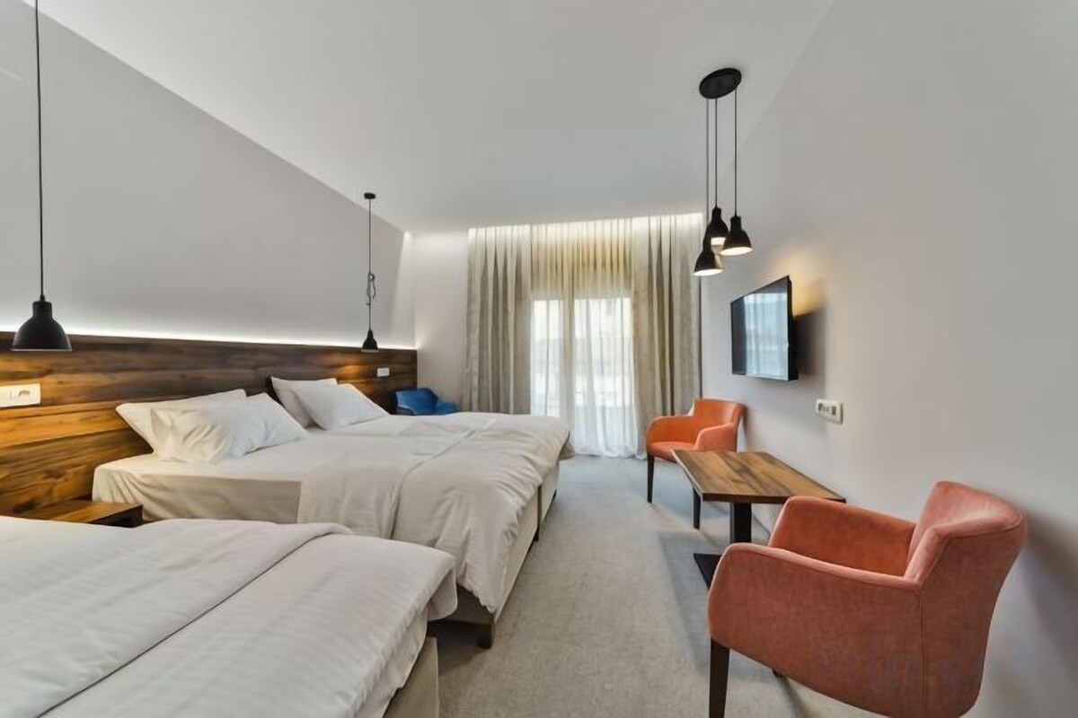 A hotel room with two beds, a desk, a chair, a TV, and a window with curtains.