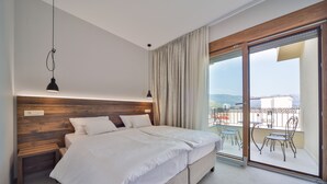 A modern bedroom with a large bed, wooden headboard, and a view of a balcony with outdoor furniture.