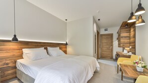 A modern bedroom with a large bed, wooden headboard, and a dining area with yellow chairs and a wooden table. - Hotel Vladimir (Budva)