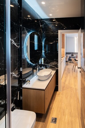 A modern bathroom with a large mirror, black marble walls, and a wooden vanity.