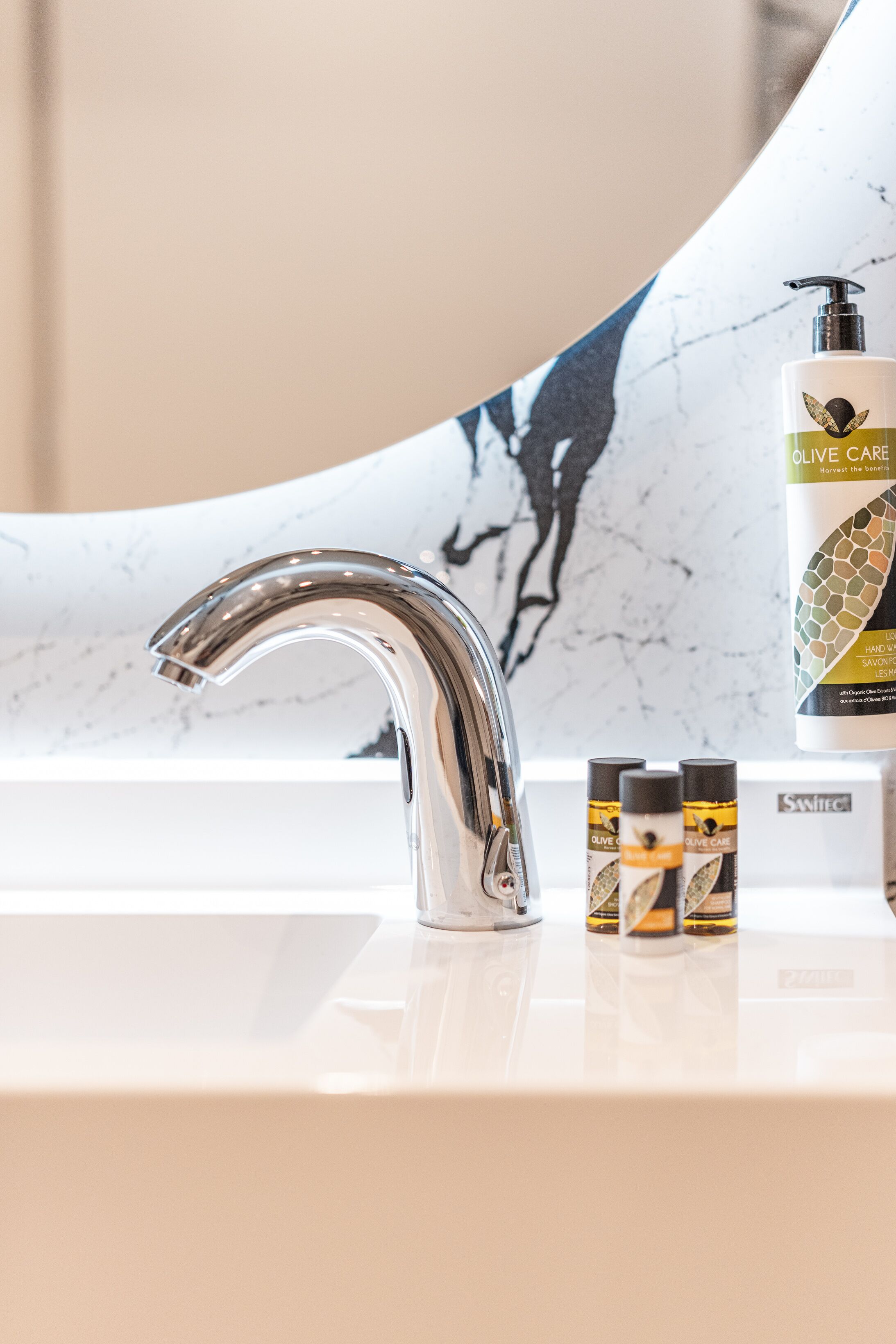 A modern bathroom with a chrome faucet, a marble sink, and a bottle of olive oil on the counter.