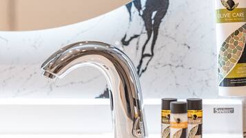 A modern bathroom with a chrome faucet, a marble sink, and a bottle of olive oil on the counter.