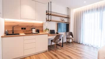Una cocina moderna con encimera de madera, armarios blancos y una cafetera integrada. Hay un ordenador portátil sobre la encimera y una silla delante.