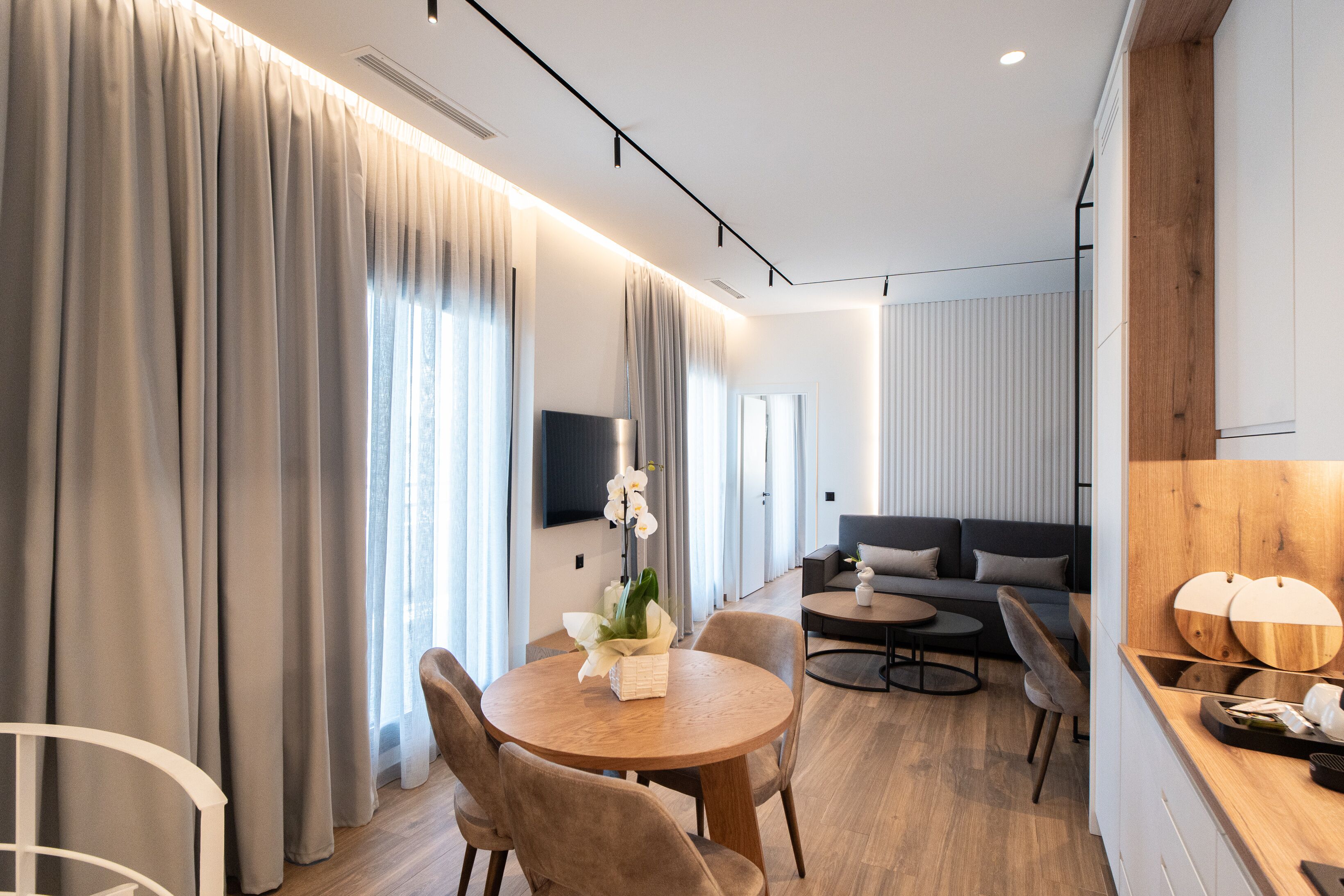 Una habitación de hotel moderna con zona de comedor, sofá y un muro decorativo de madera.