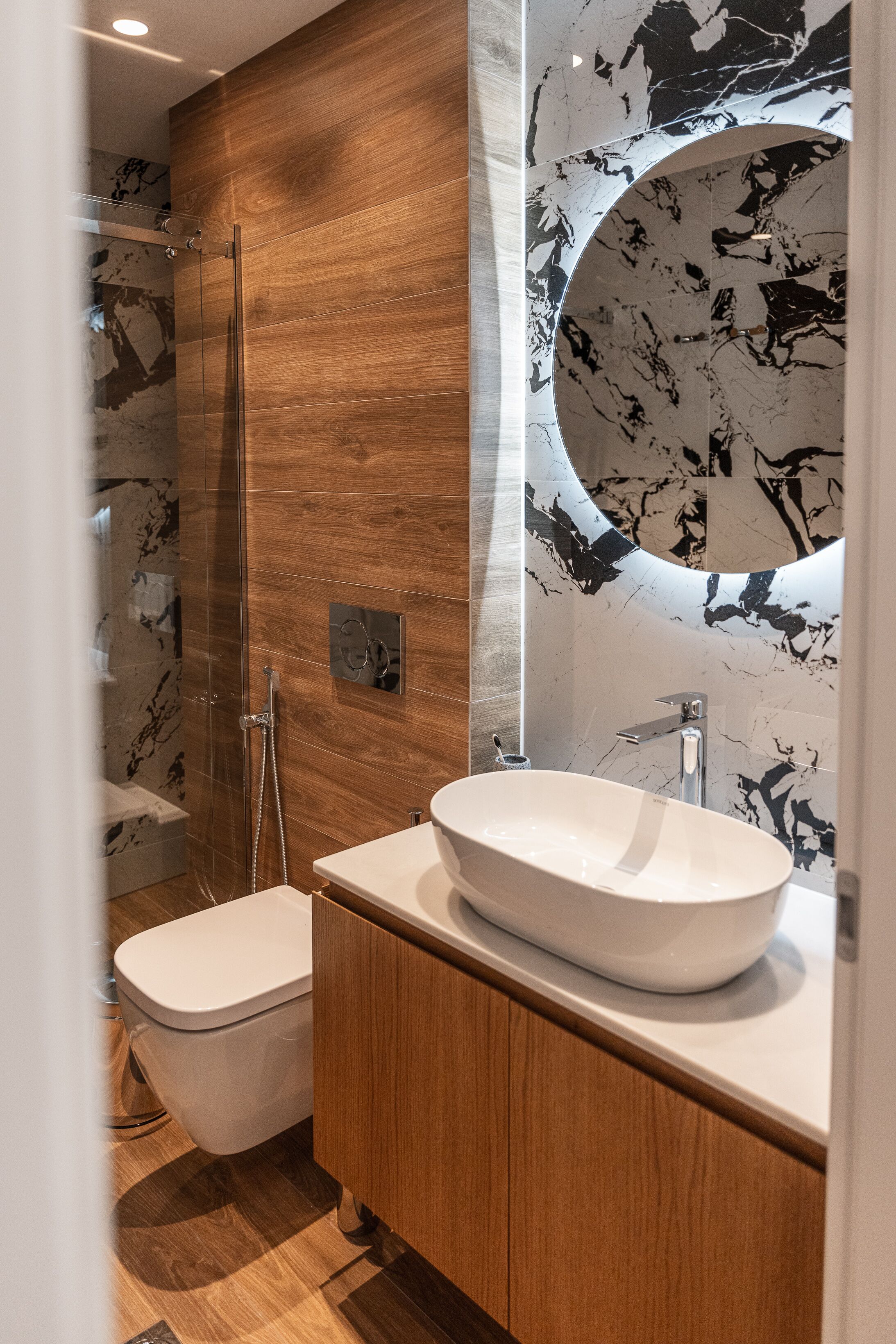 A modern bathroom with a wooden vanity, a freestanding toilet, and a glass-enclosed shower.