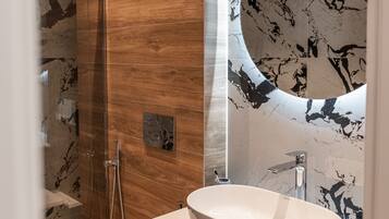 A modern bathroom with a wooden vanity, a freestanding toilet, and a glass-enclosed shower.
