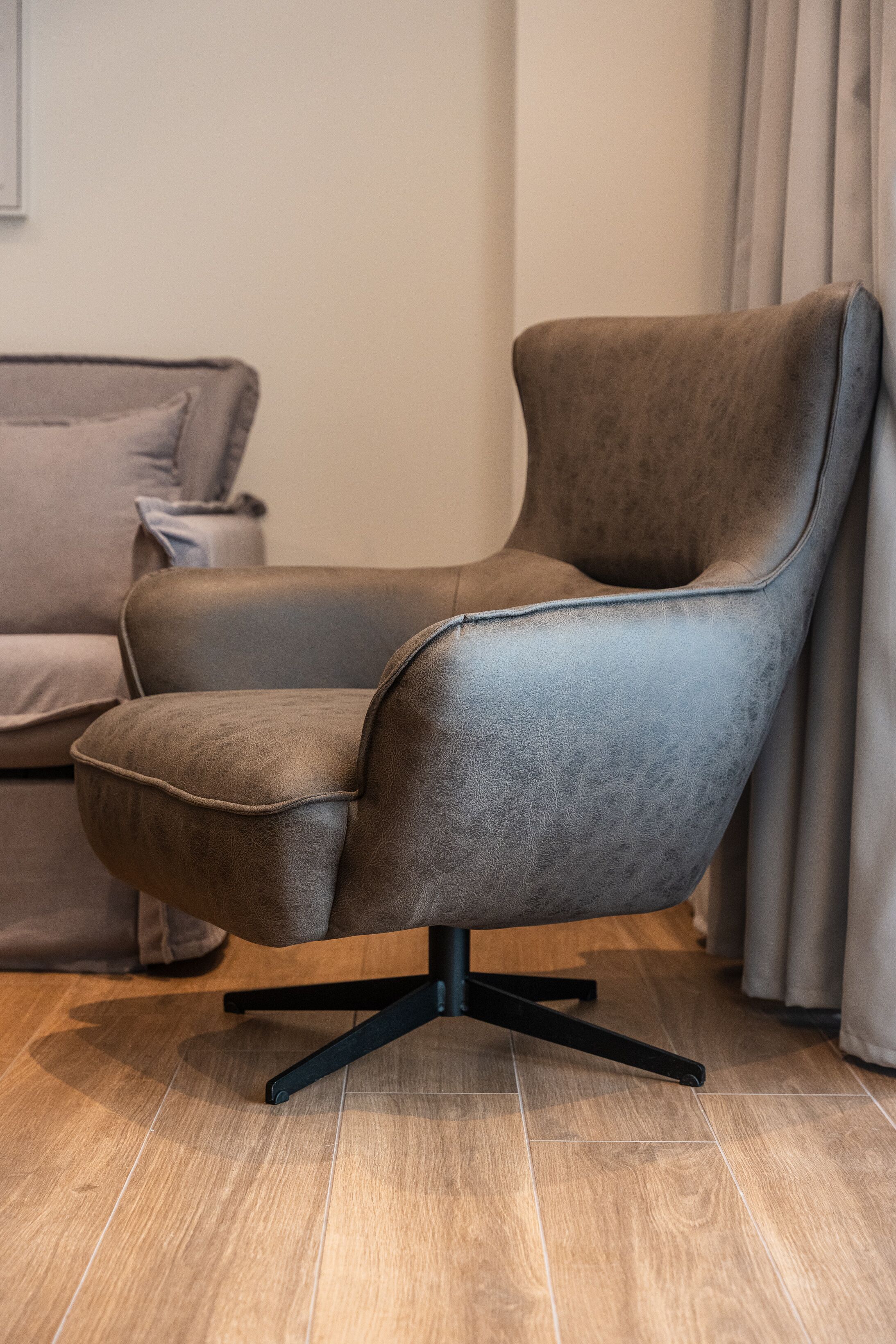A modern armchair with a high backrest and a swivel base, positioned on a wooden floor.