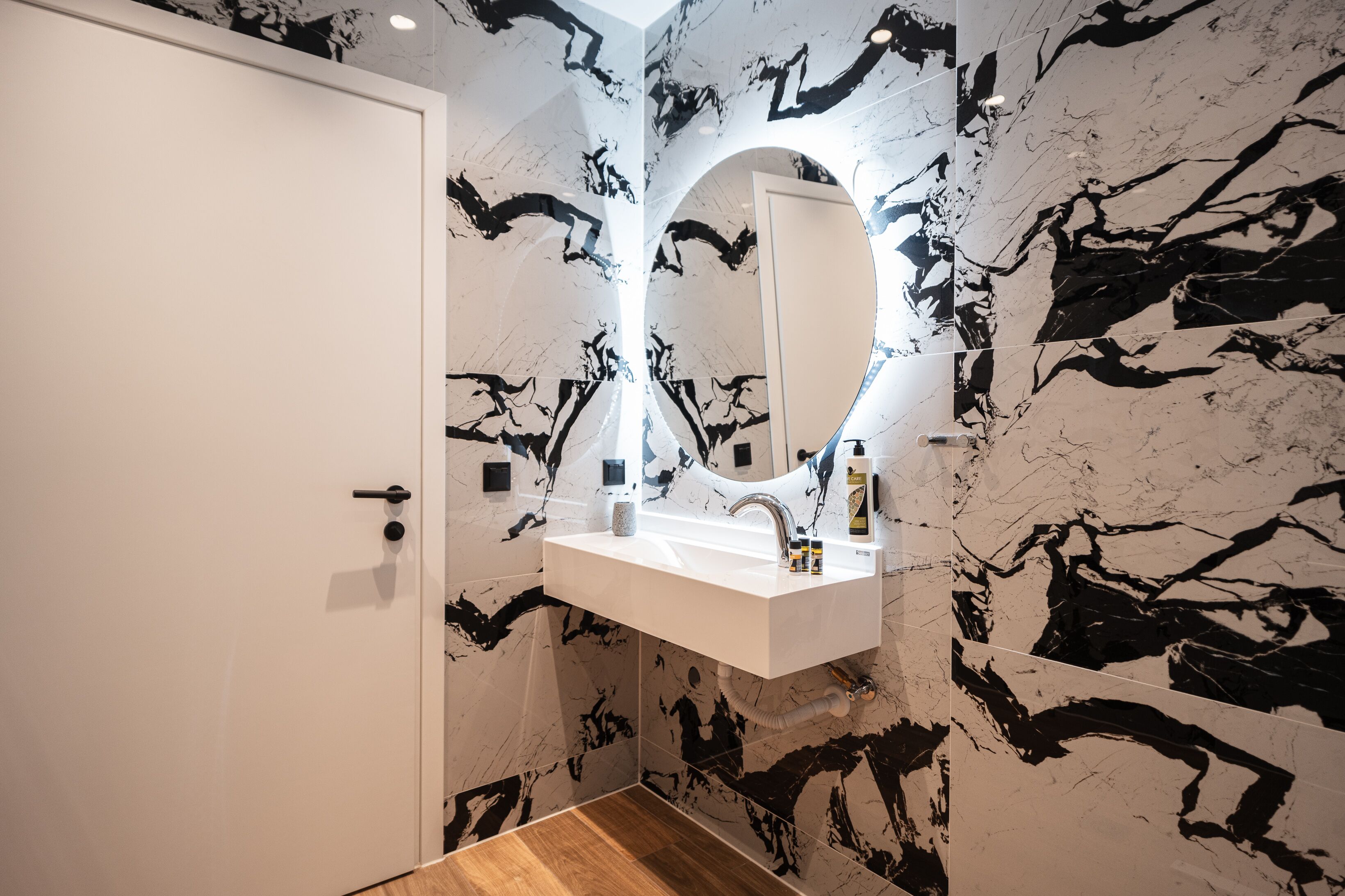 Un baño con tocador blanco, espejo y paredes de mármol negro.