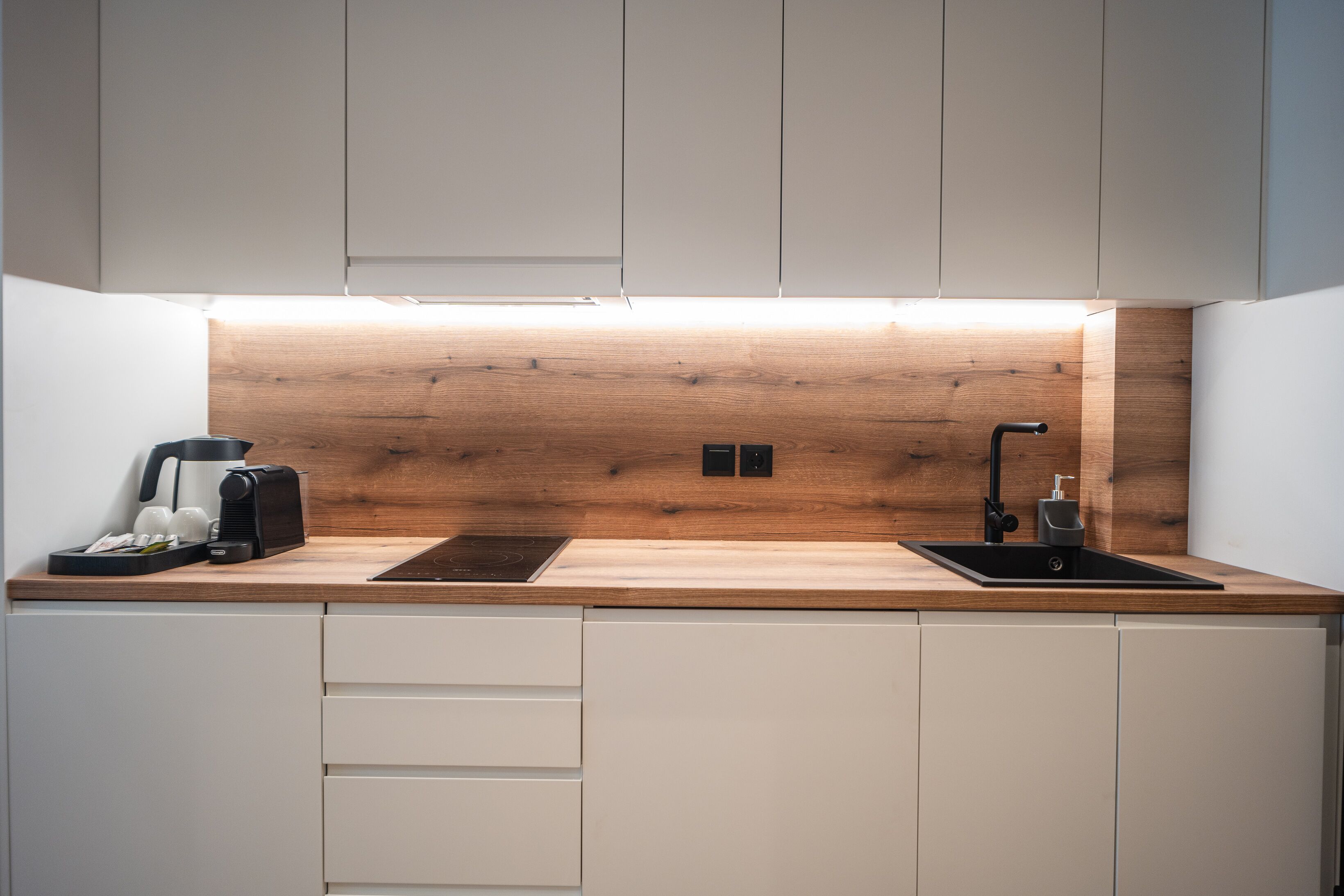 Una cocina moderna con protector contra salpicaduras de madera, un lavamanos negro y una cafetera.