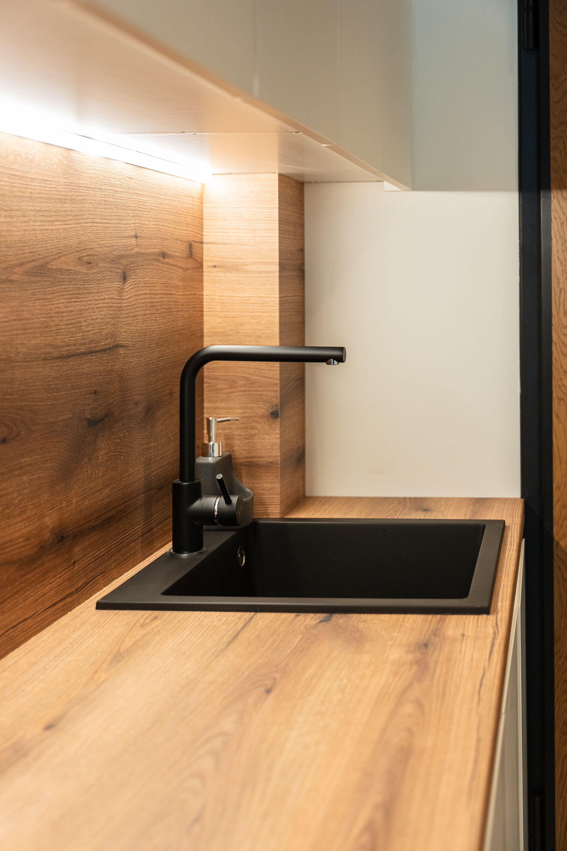 Una cocina moderna con un lavamanos negro, encimera de madera y grifo negro.