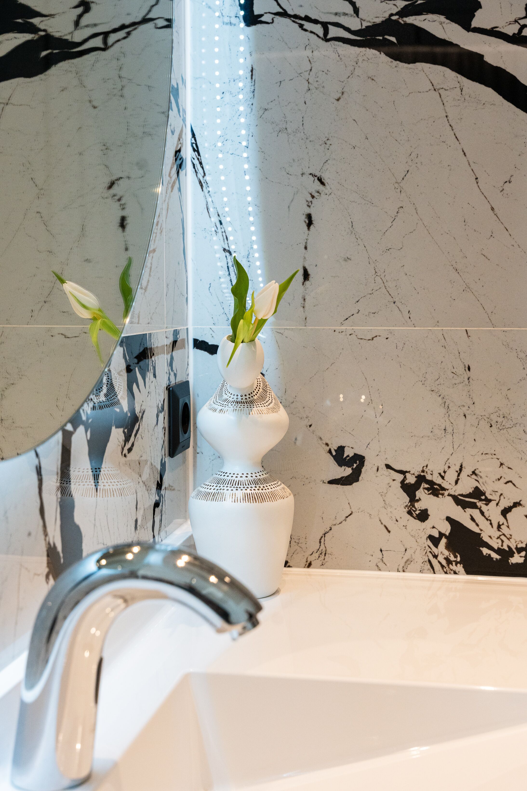 Een badkamer met een wit wastafelmeubel, een spiegel en een vaas met een plant.