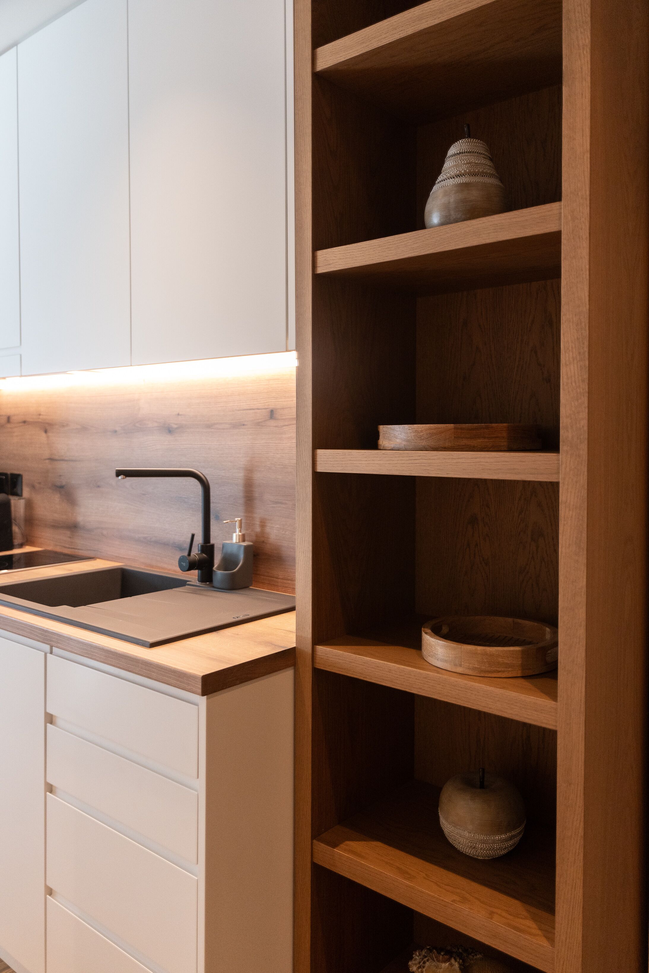 A kitchen with a wooden shelf unit, a modern faucet, and a white cabinet.