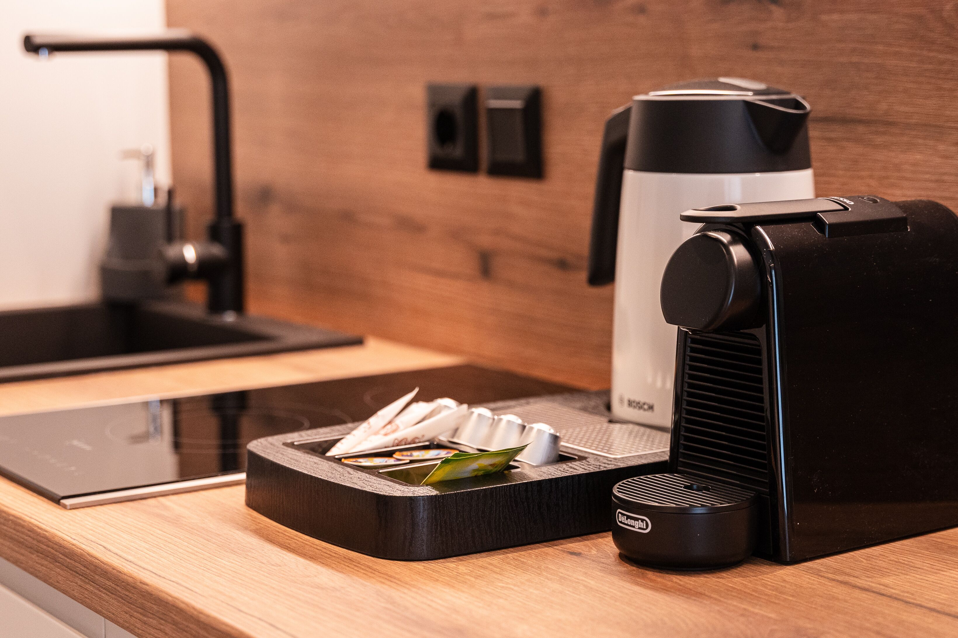 A modern kitchen with a coffee machine, a kettle, and a tea kettle on a wooden countertop.