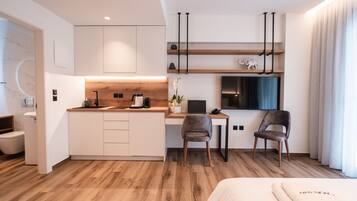 A modern hotel room with a kitchenette, a desk, a chair, a bed, and a bathroom.