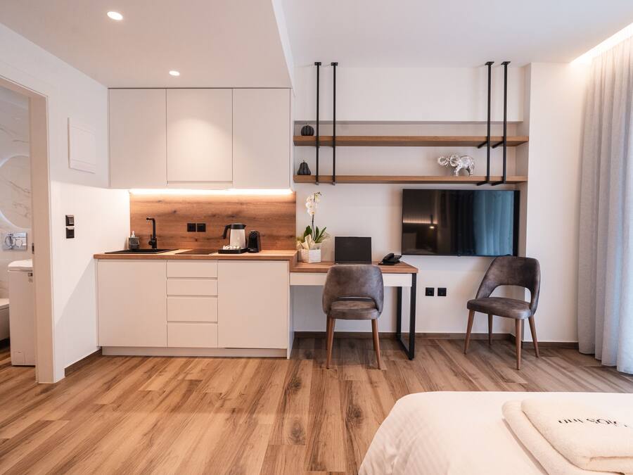 A modern hotel room with a kitchenette, a desk, a chair, a bed, and a bathroom.