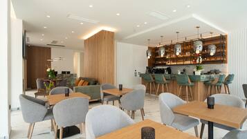 Een moderne eetruimte met houten tafels en grijze stoelen, een bar met flessenrekken en een houten accentmuur.